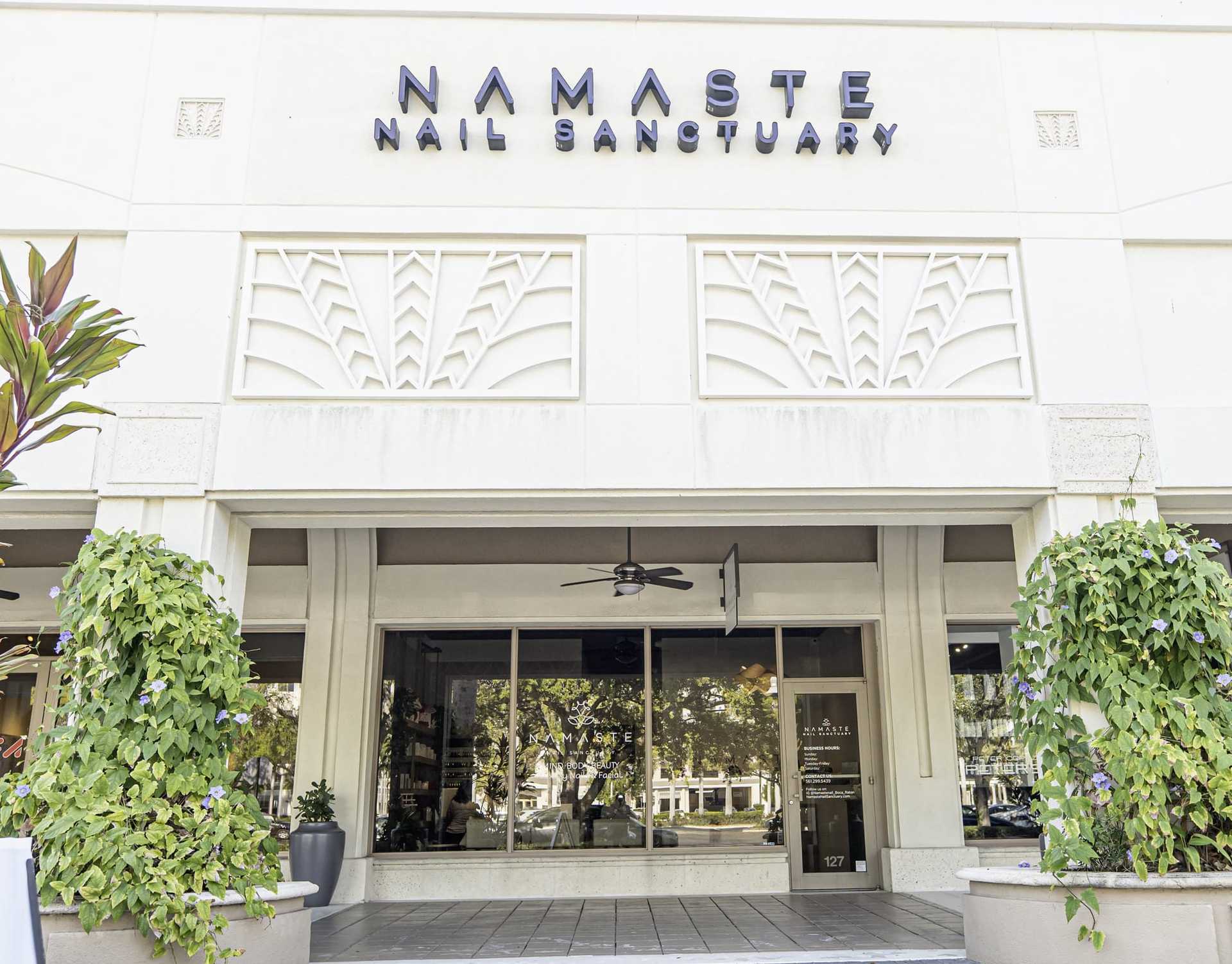 Nail salon entrance with greenery and modern signage reading 'Namaste Nail Sanctuary'.