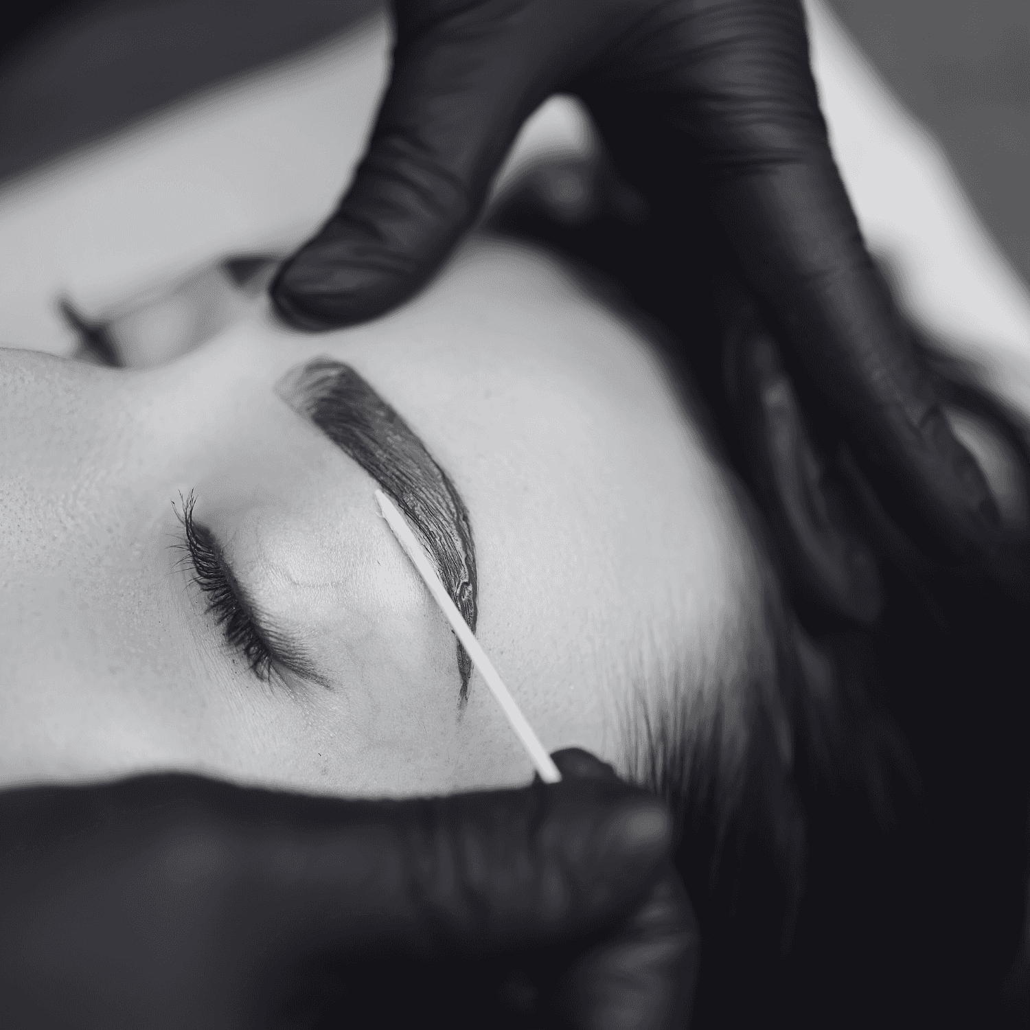 Eyebrow grooming using a cotton swab, person wears black gloves, close-up view.