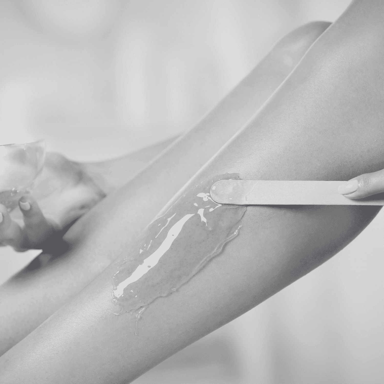 Applying wax on a person's leg with a wooden spatula for hair removal.